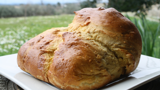 A large, golden-brown loaf of bread on a white plate outdoors.