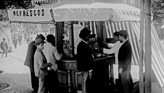 Historic photo of people at a street refreshment stand with striped canopy.