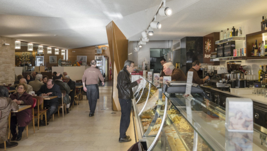 People dine in a cafe with a pastry display and bar counter.