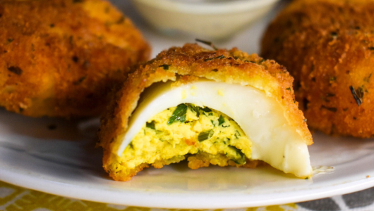 Close-up of breaded, stuffed appetizer with cheese and herbs inside on a white plate.