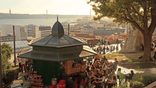 People sitting at a hilltop cafe with city and water views in the background.