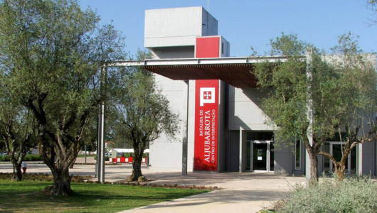 Modern building entrance with red vertical sign and olive trees around.