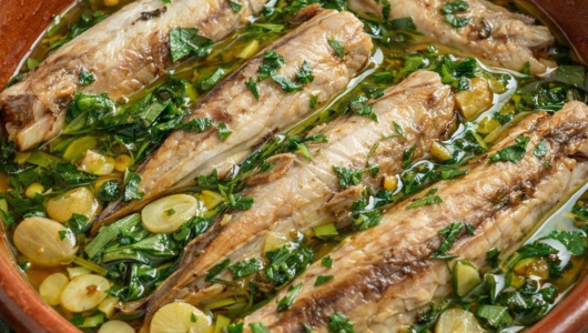 Four cooked fish in a dish with herbs and sliced vegetables.