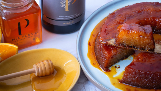 Caramelized cake on a plate with honey jar, honey dipper, and an orange slice.