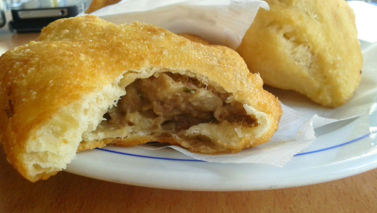 Two pastries on a plate, one with a visible meat filling.