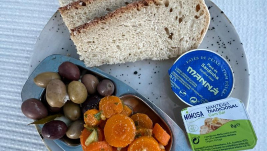Plate with bread, mixed olives, carrot salad, and butter containers.
