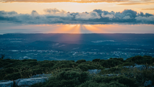 Sunset over hilly landscape with rays and clouds.