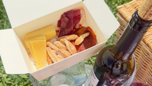 Box with cheese, cured meats, breadsticks, and wine bottle beside.