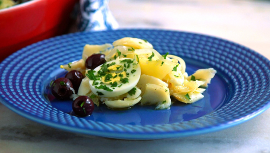 Plate with sliced potatoes, olives, and herbs on top.
