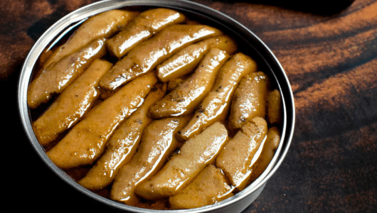 Opened can of pickled mushrooms in liquid on a wooden surface.