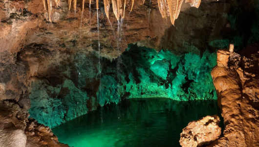 Cave interior with stalactites and emerald-lit water.