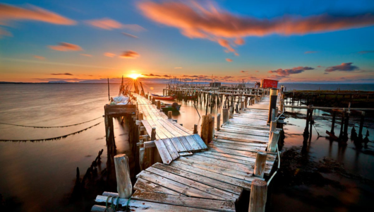 Sunset over weathered wooden pier extending into calm sea.