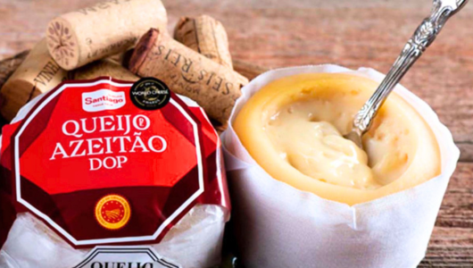 Soft cheese in a white wrap with a spoon and corks on a wooden surface.