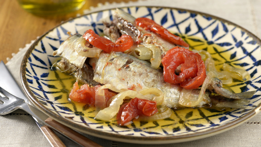 Plate with cooked fish, tomato slices, and onions on a patterned dish.
