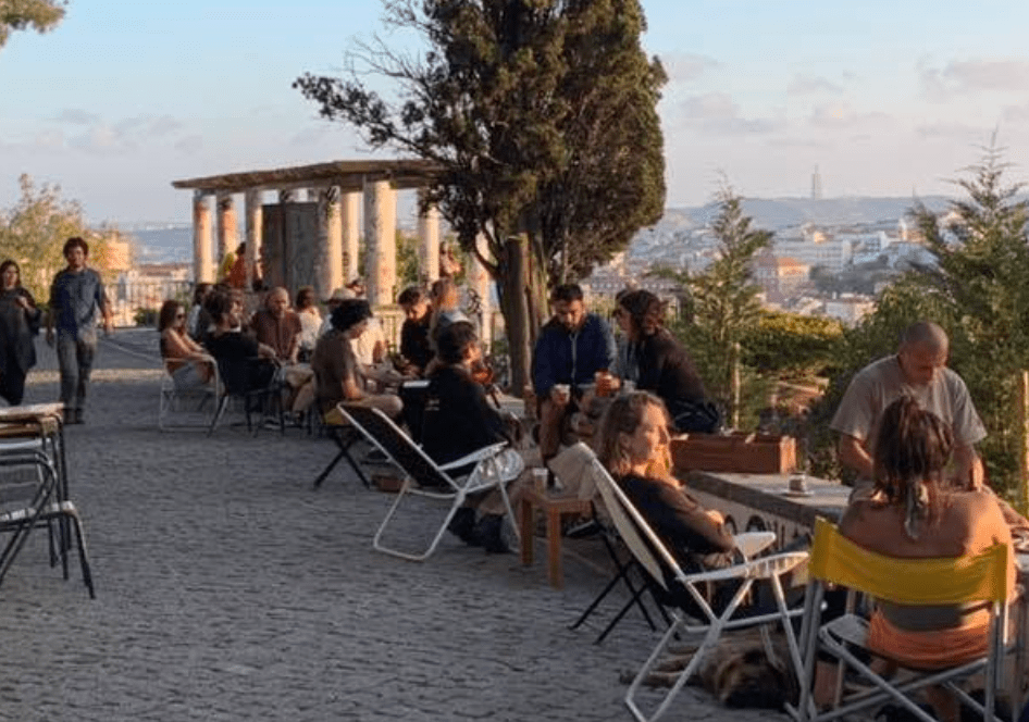 People sitting at outdoor tables on a cobblestone patio with distant city views.