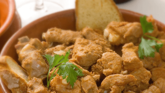 A dish of cooked chicken pieces garnished with parsley and served with bread.
