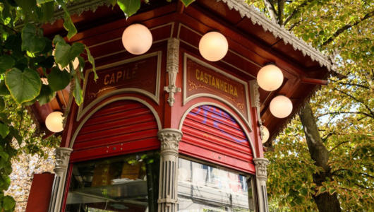 Red kiosk with round lights, surrounded by trees.