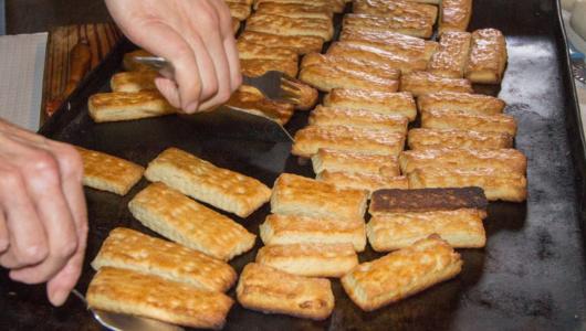 Person flipping rectangular fried food pieces on a griddle.