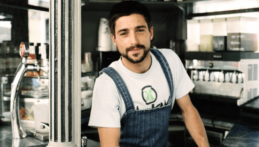 Smiling person in denim overalls at a café counter.