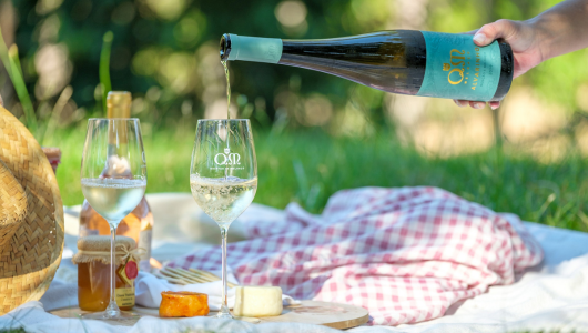 Wine being poured into a glass on a picnic blanket with cheese and honey.