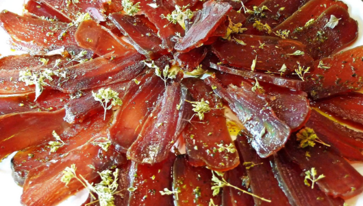 Sliced cured meat arranged in a circular pattern, garnished with herbs.