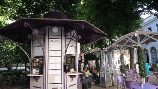 Outdoor kiosk with seating area under umbrellas, surrounded by trees.