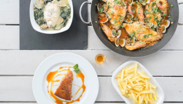 Dishes with fish, clams, fries, and sauce on a white table.