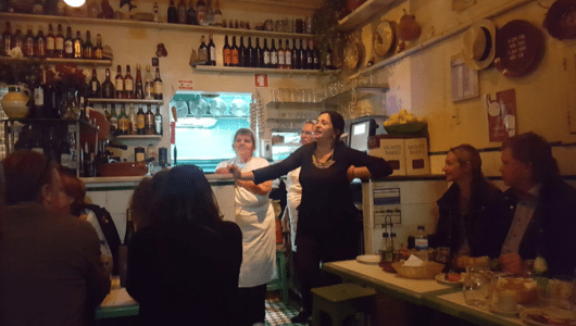 People in a cozy restaurant with wine bottles and decorations on shelves.