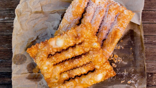 Two sugar-dusted fried pastries on parchment paper