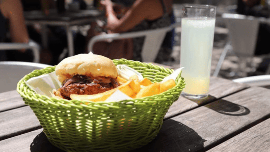 Burger and fries in basket with lemonade on outdoor table.