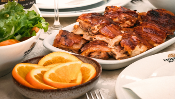 Plate of roasted chicken and sliced oranges on a table with salad.