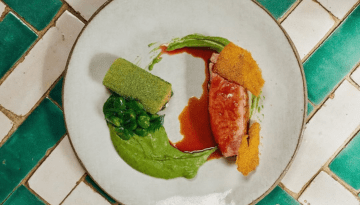 Gourmet dish with meat, green puree, leafy greens, and sauce on decorative plate.