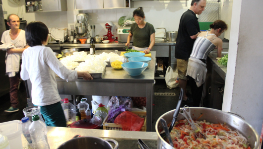 Five people preparing food in a busy kitchen with bowls and ingredients.