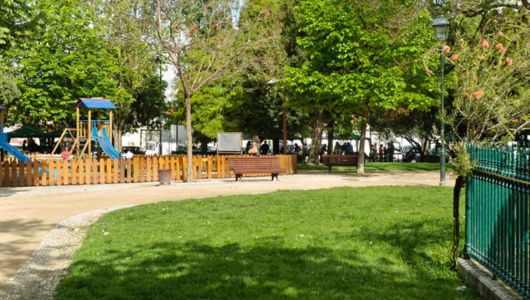 Sunny park scene with playground, benches, and green grass.