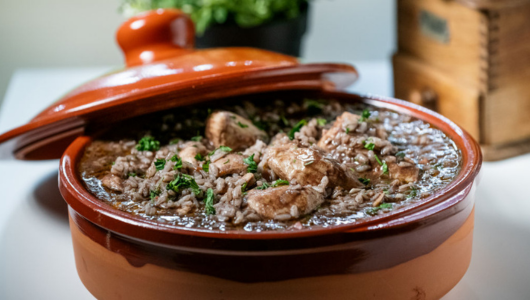 Clay pot with rice and meat topped with herbs.