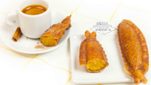 Cup of espresso with fried pastries on a plate.