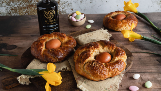 Three breads with eggs in center, flowers, colored candies, and a bottle on a wooden surface.