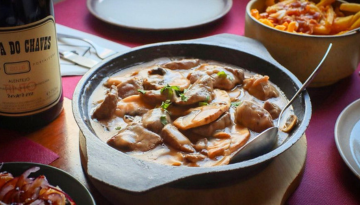 Creamy mushroom stew in pan, wine bottle, and pasta on table.