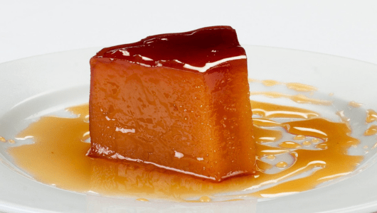 Slice of caramel flan on a plate with syrup.