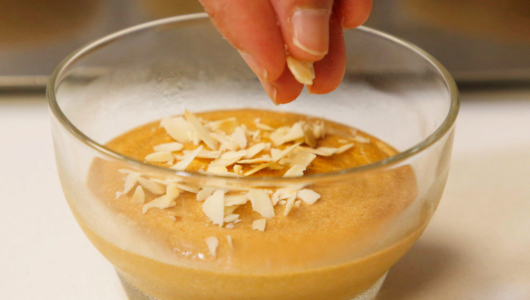 Hand sprinkling coconut flakes on a dessert in a glass bowl.