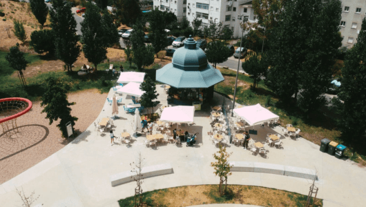 Aerial view of an outdoor café with tables and umbrellas near trees and buildings.