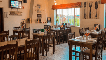 Cozy restaurant interior with wooden tables and chairs, wall art, and bright window.