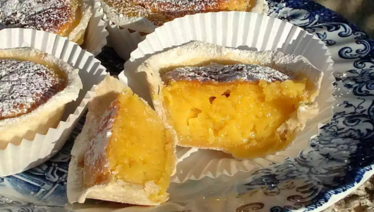 Delicious custard tarts with golden filling and flaky crust, served in paper cups on a blue-patterned plate.
