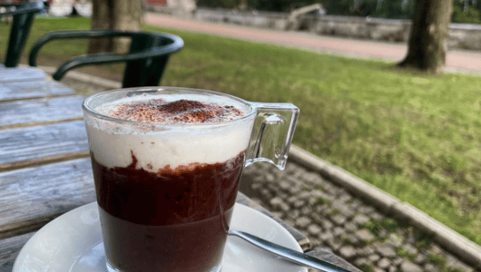 Glass cup of hot chocolate with cream on outdoor table.