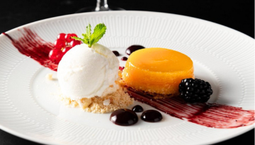 Plated dessert with ice cream, red sauce, a yellow tart, and fruit garnish.