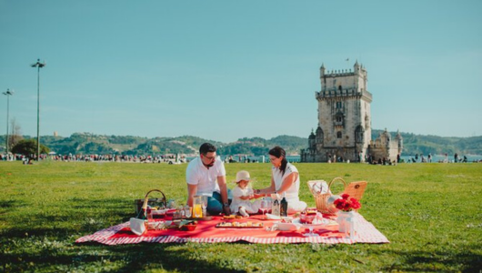 Family enjoying a picnic on grass near a historic tower on a sunny day.