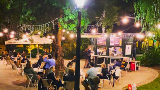 Outdoor cafe at night with people seated under string lights.