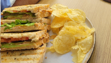 Grilled sandwiches with lettuce and tomatoes beside potato chips on a plate.