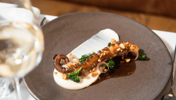 Gourmet dish with grilled octopus, sauce, greens on a plate.
