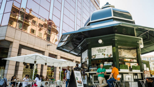 People sitting around a modern street kiosk near a glass building.